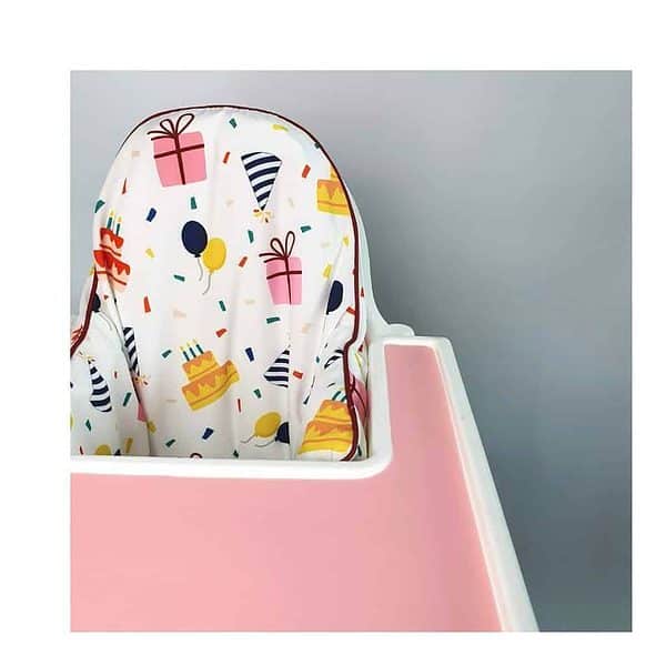A pink high chair with a birthday theme.