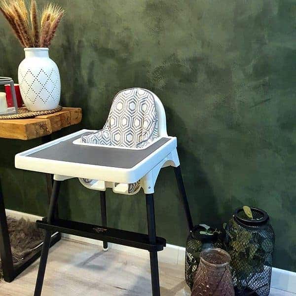 A high chair in front of a green wall.