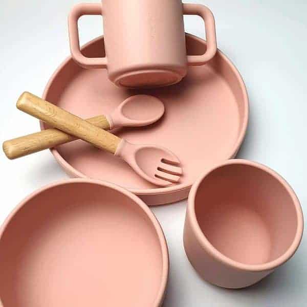 A set of pink plates, cups and spoons on a white surface.